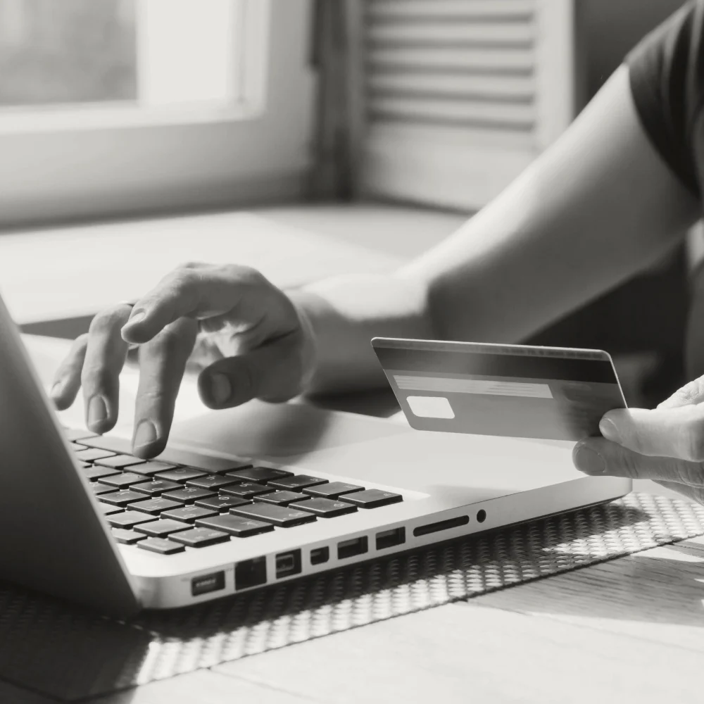 A person's hand typing on a laptop keyboard while the other hand holds a debit or credit card.