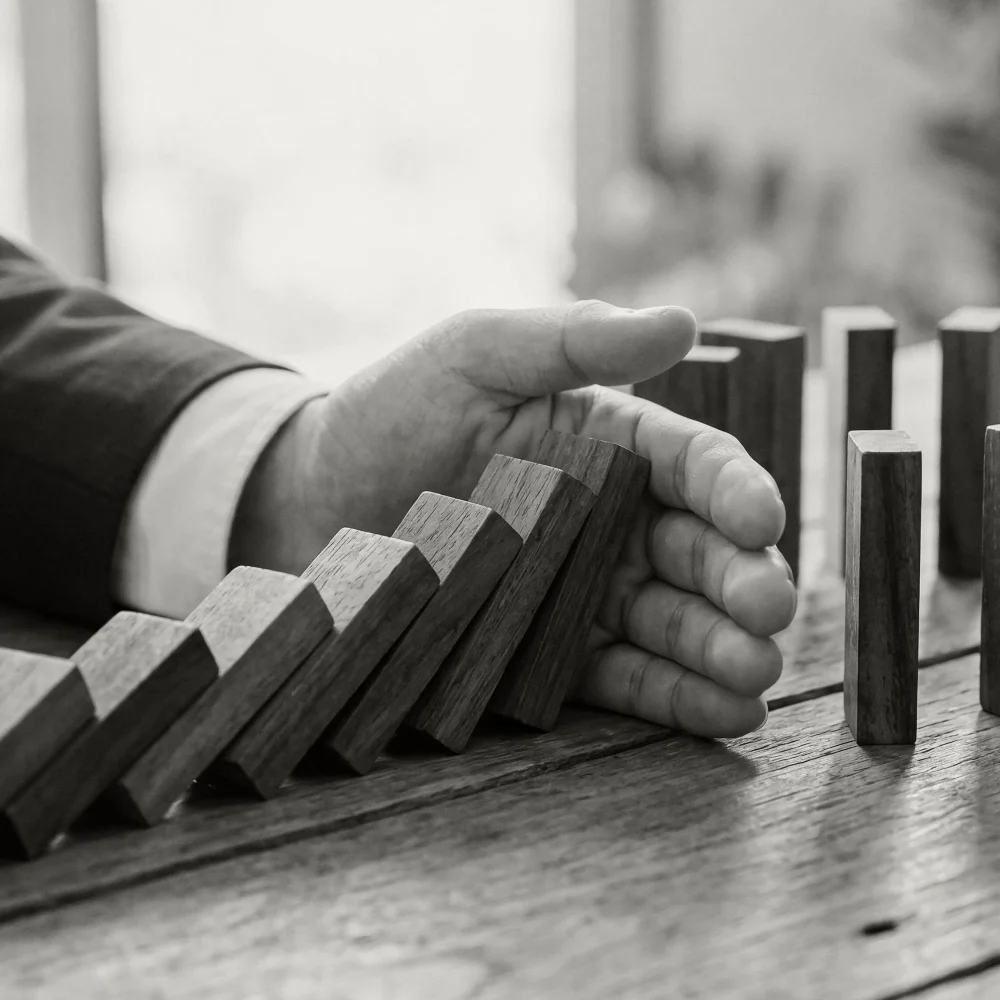 A man in a suit blocks a row of falling wooden dominoes.