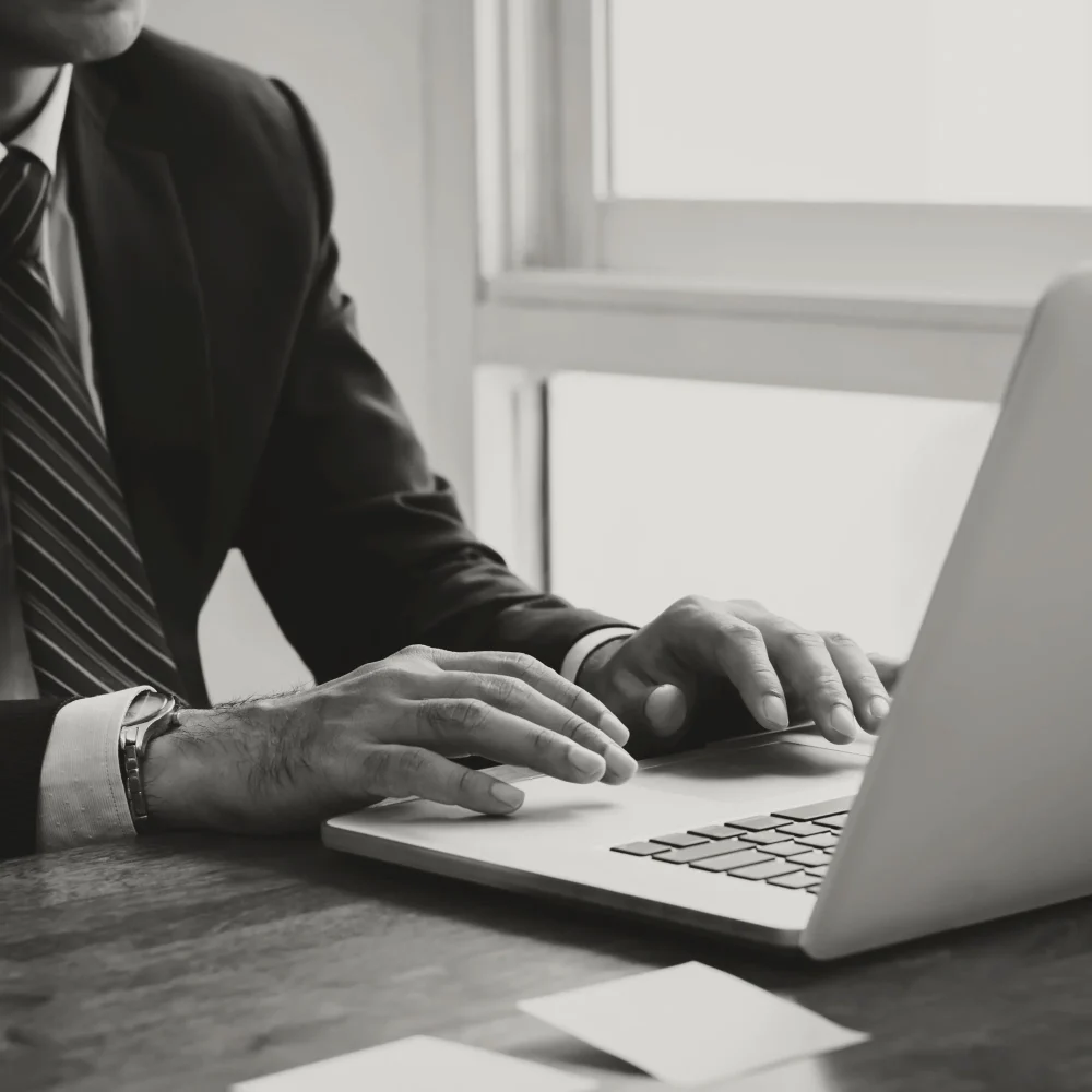 A person wearing a suit and tie using a laptop on a wooden desk.