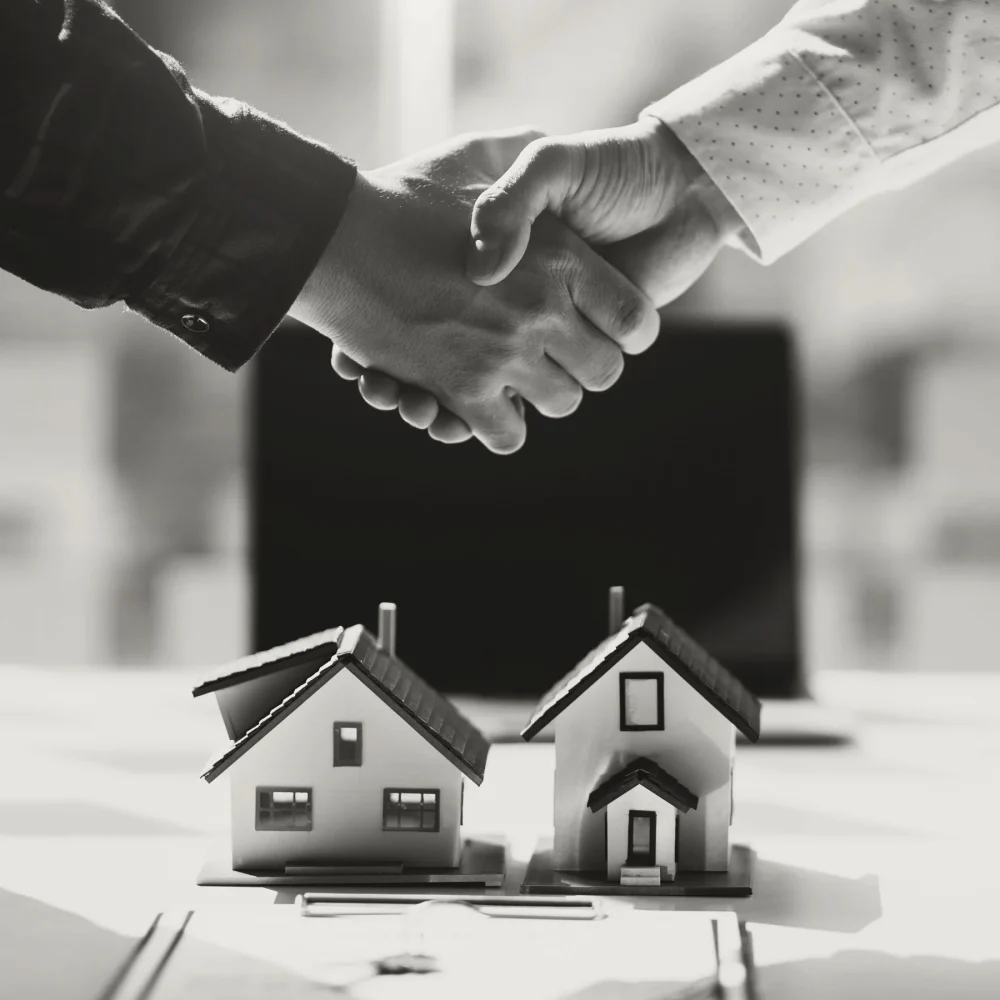 Two people shaking hands above two models of houses.